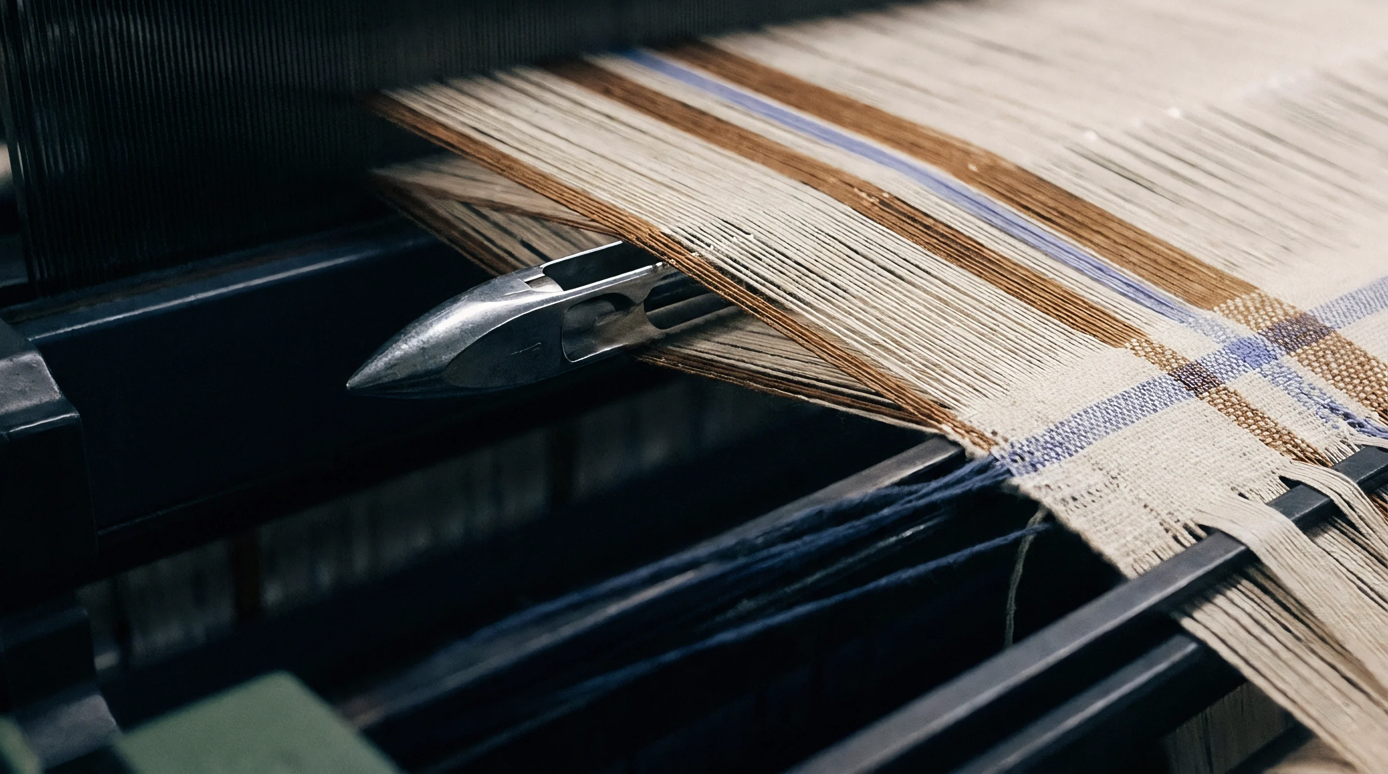 Precision metallic loom shuttle inserts filling yarn across separated warp threads during industrial textile weaving operations.